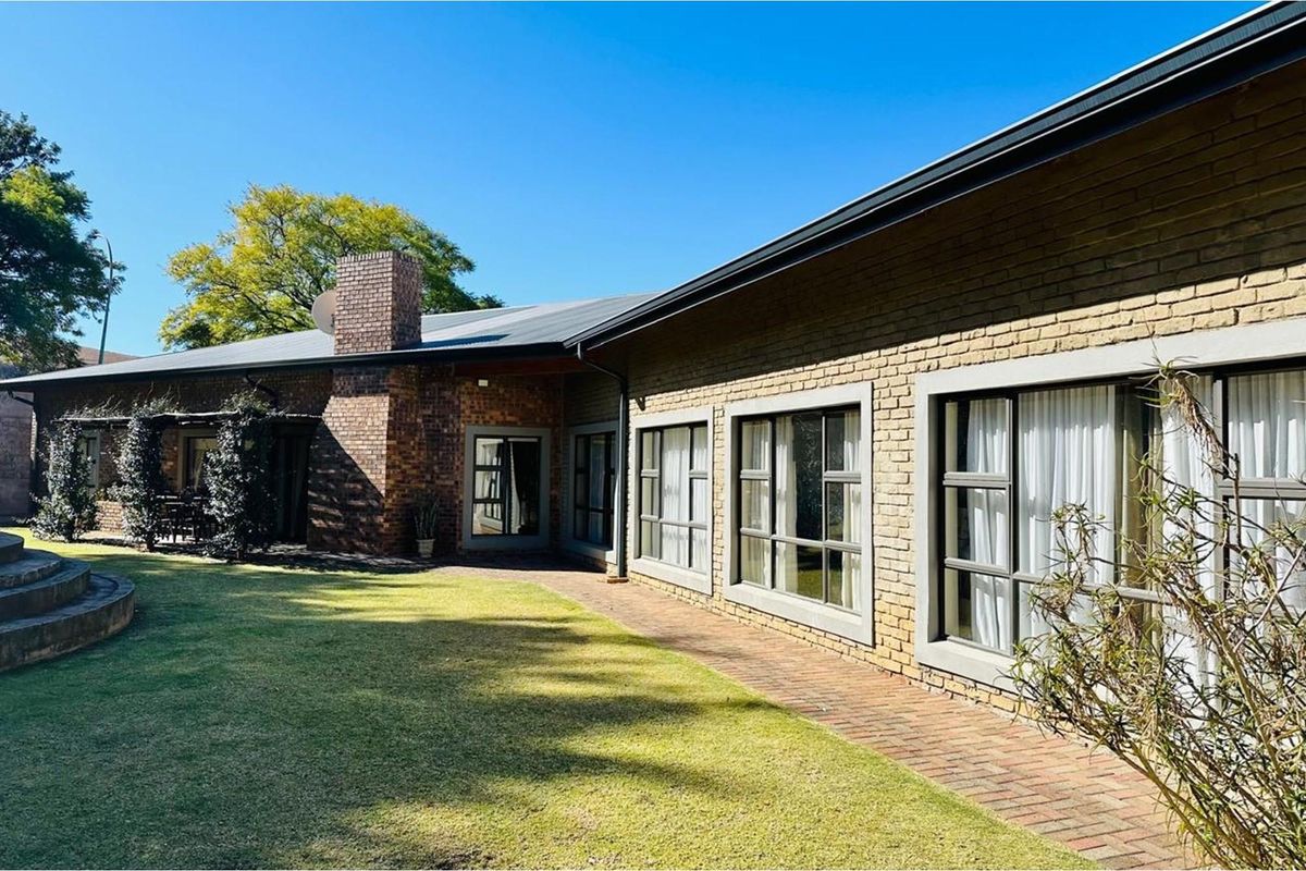 A well-maintained rear exterior view of the house featuring a brick facade, large windows, a brick chimney, and a paved walkway leading to the garden.