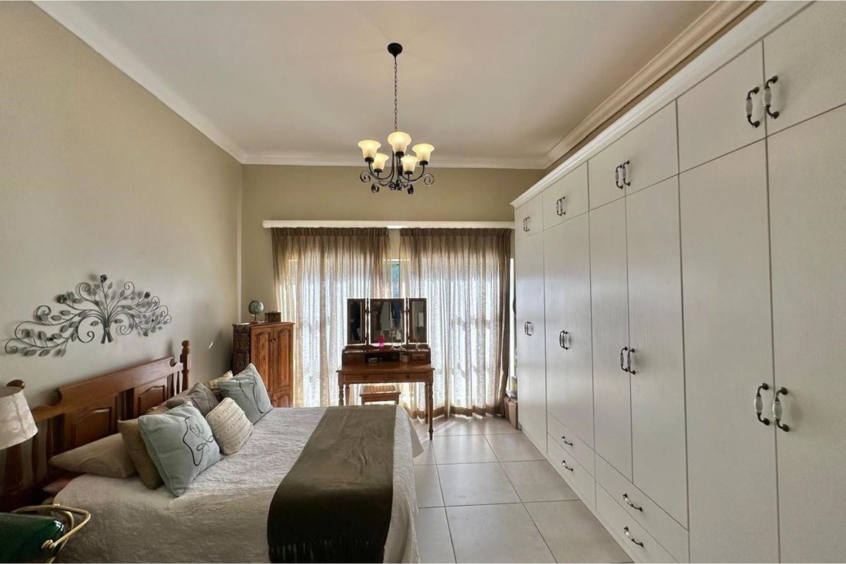A well-maintained bedroom featuring extensive floor-to-ceiling built-in cabinetry, tiled flooring, and a classic chandelier, offering ample storage and a neutral aesthetic.