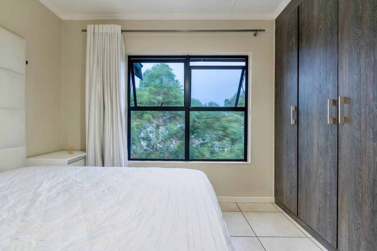 A well-maintained bedroom featuring built-in dark wood-grain wardrobes, tiled flooring, and a large window providing natural light and exterior views.