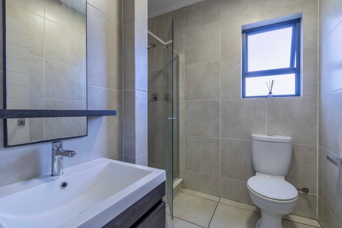 Modern bathroom featuring a glass-enclosed shower, wall-mounted vanity with basin, and a contemporary toilet, finished with neutral floor-to-ceiling tiling.