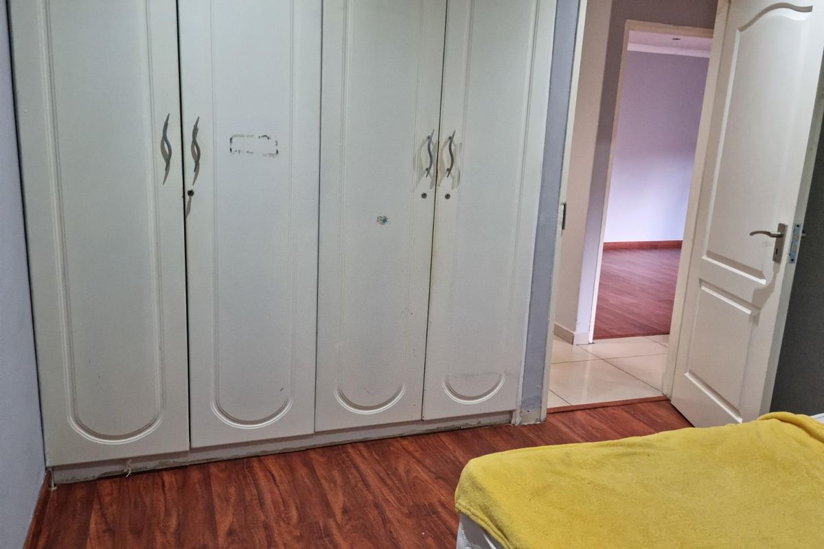 Bedroom featuring built-in white wardrobes, laminate wood flooring, and a doorway leading to an adjacent room.