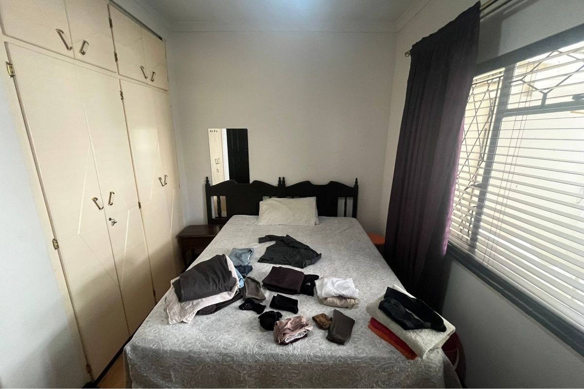 A functional bedroom featuring built-in cupboards and security bars on the window, providing a practical and secure living space.