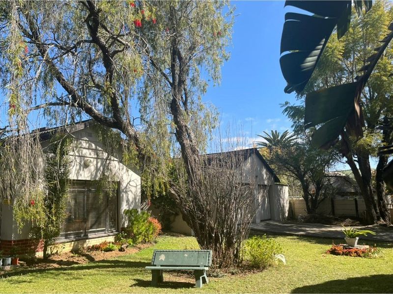A spacious rear garden featuring a well-maintained lawn, mature trees, and a paved driveway leading to the property.