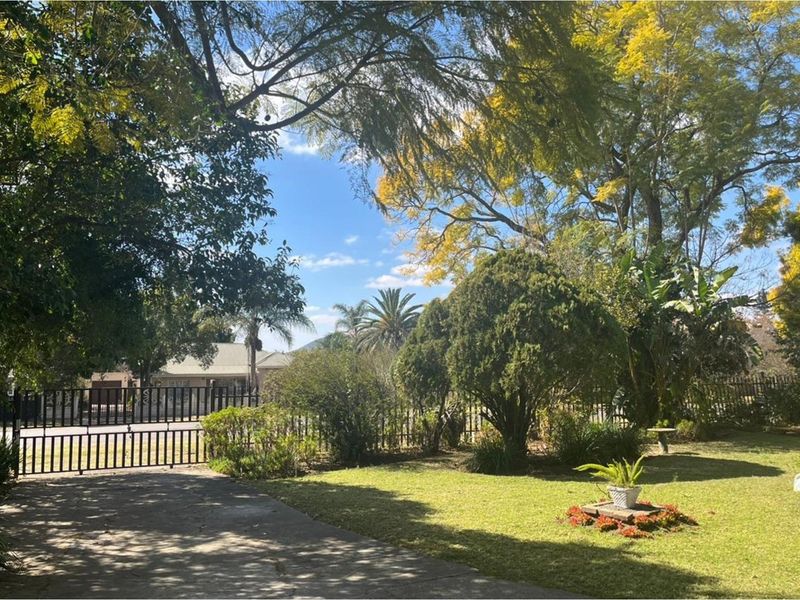 A view of the front garden featuring a concrete driveway, established trees, and a secure metal gate entrance.