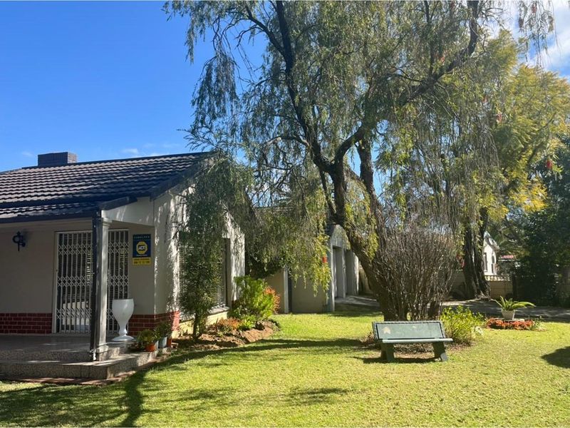A view of the rear garden featuring a covered patio, brick and plaster facade, and established trees.
