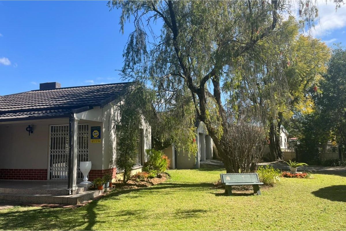 A view of the rear garden featuring a covered patio, brick and plaster facade, and established trees.