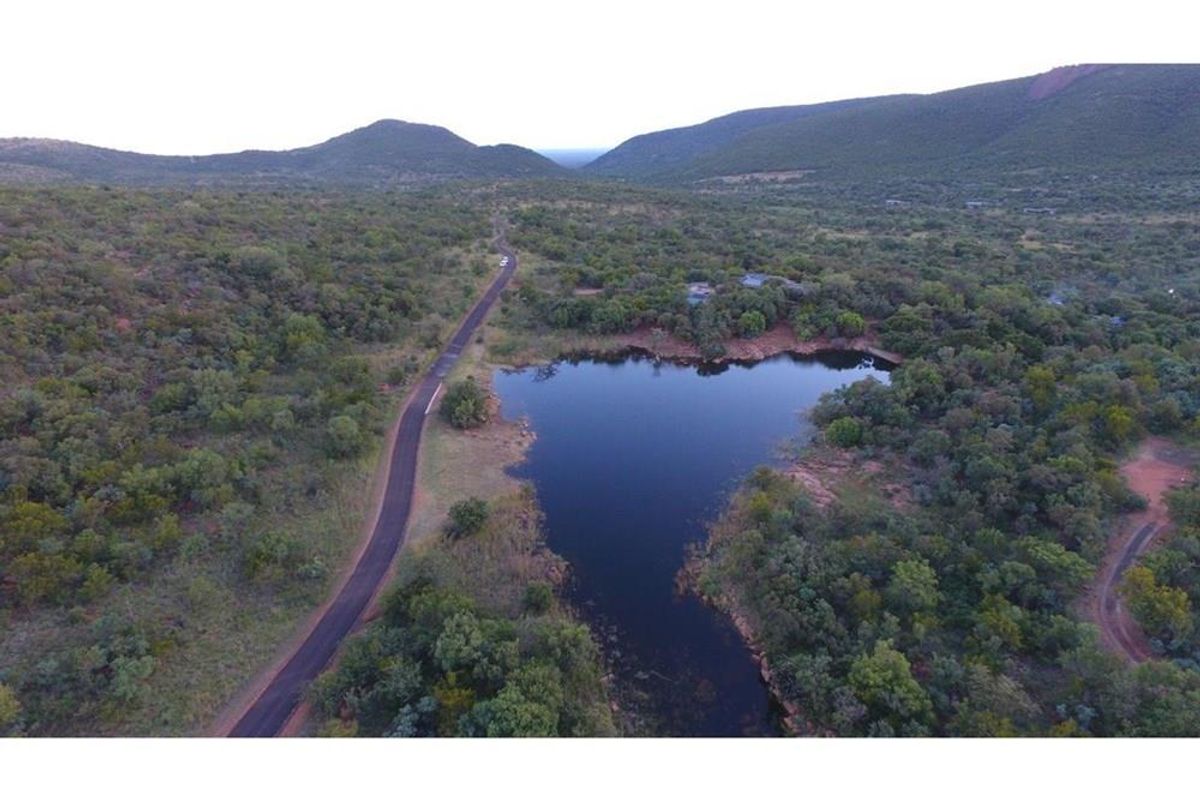 An aerial view of a vacant residential plot featuring natural landscape, indigenous vegetation, and a scenic water body with access road.