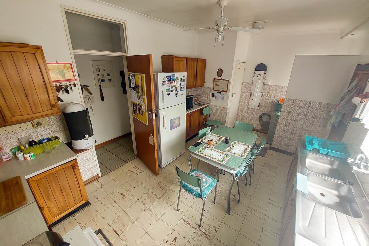 A dated kitchen featuring wooden cabinetry, tiled flooring, and a double basin sink, offering a functional space with potential for modernization.