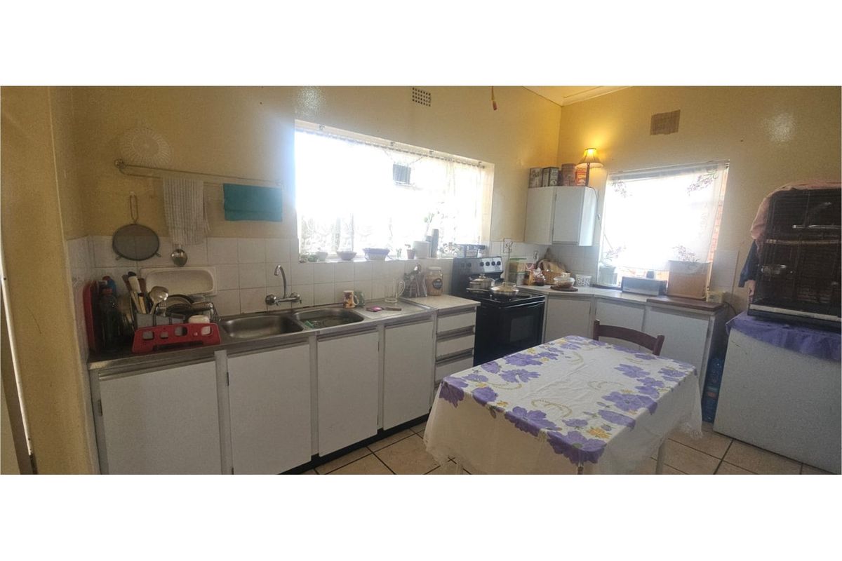 A functional kitchen featuring white cabinetry, a stainless steel double sink, and a freestanding stove, offering a practical layout with natural light.