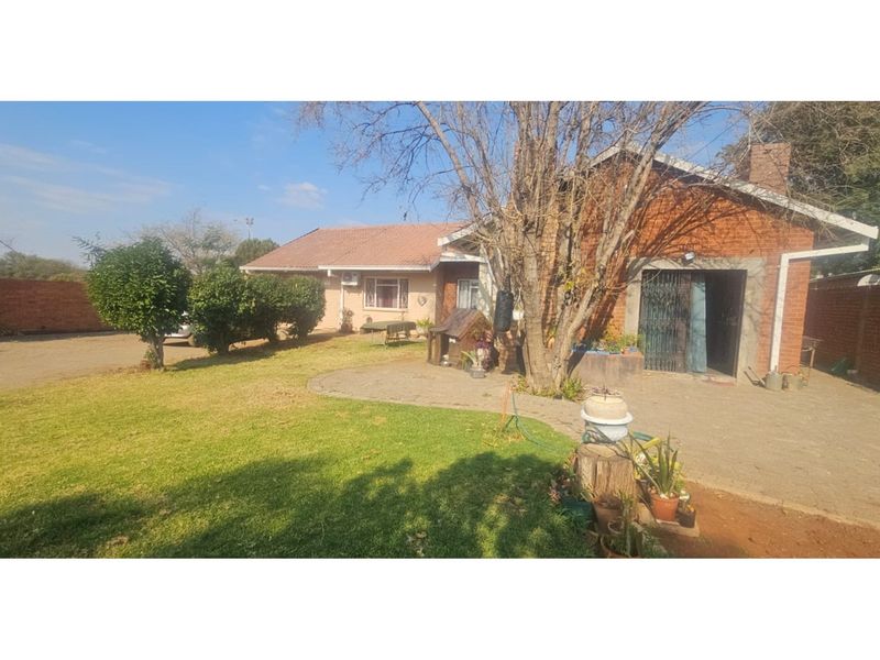 A view of the rear exterior of the house featuring a brick facade, paved patio area, and a spacious garden.