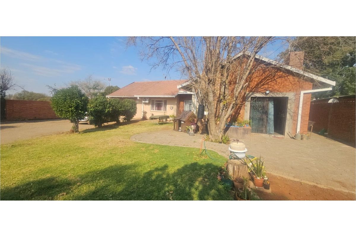 A view of the rear exterior of the house featuring a brick facade, paved patio area, and a spacious garden.