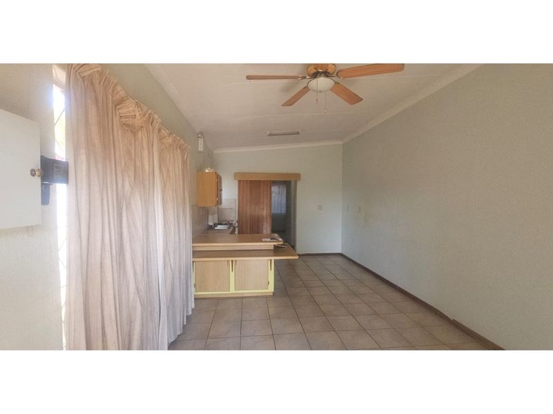Open plan living area featuring tiled flooring, a ceiling fan, and a compact kitchen area with built-in cabinetry.
