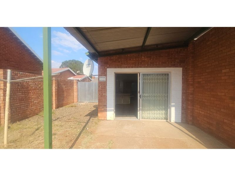 A covered patio area featuring exposed brick walls, a corrugated metal roof, and a sliding security gate leading into the interior.