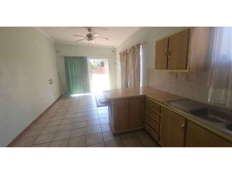 Open plan kitchen and living area featuring dated wooden cabinetry, tiled flooring, and direct access to the outdoor space via sliding doors.