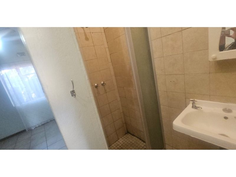 A functional bathroom featuring a tiled shower enclosure, a wall-mounted basin, and a medicine cabinet, showing signs of age and wear.