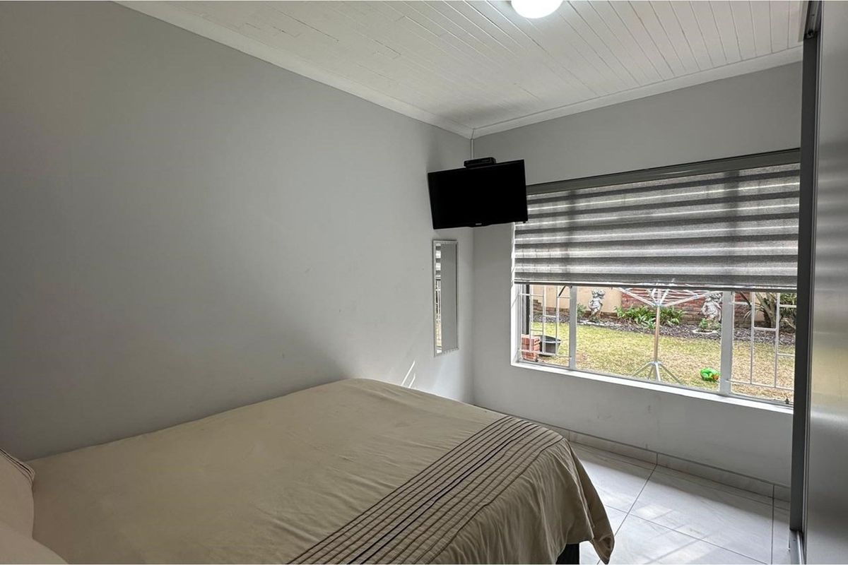 A functional bedroom featuring tiled flooring, a tongue and groove ceiling, and a built-in wardrobe with a view of the rear garden.