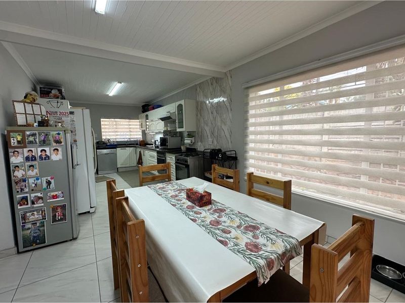 Open-plan kitchen and dining area featuring tiled floors, built-in cabinetry, and modern roller blinds, creating a functional and connected living space.