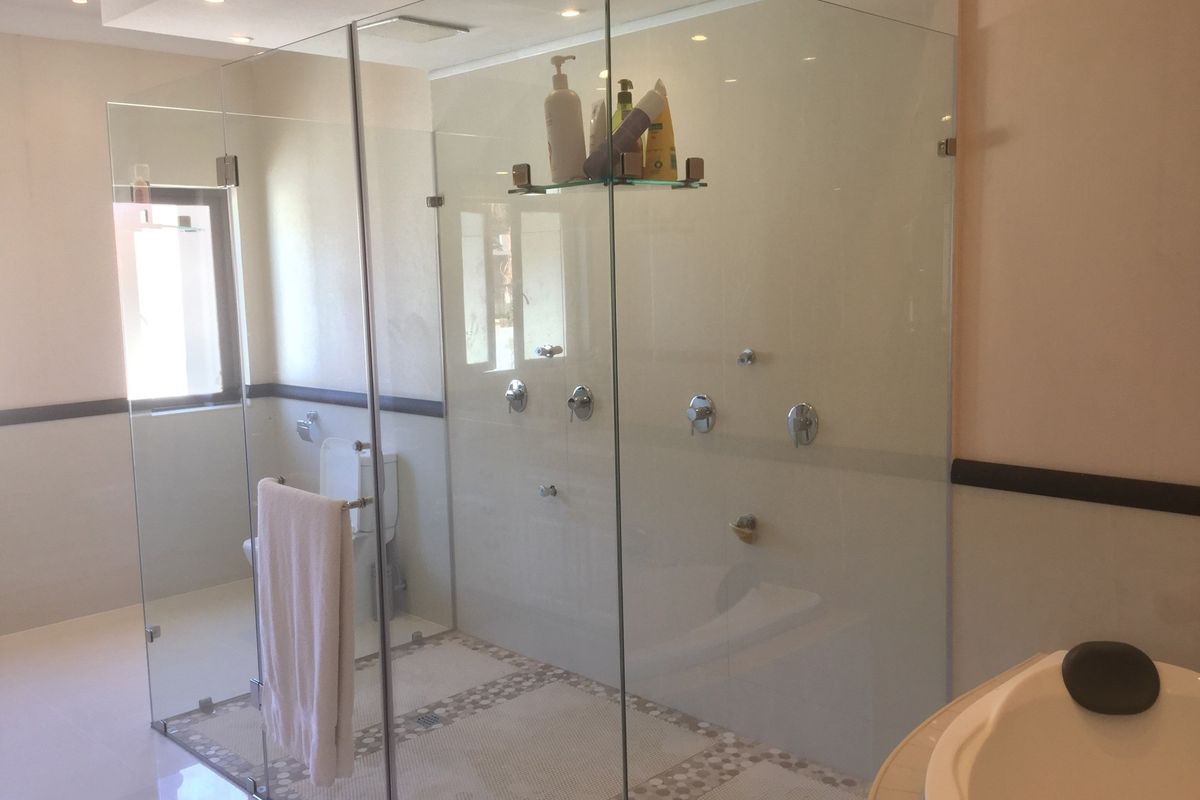 A modern bathroom featuring a large walk-in glass shower enclosure with multiple shower heads and mosaic tile flooring.