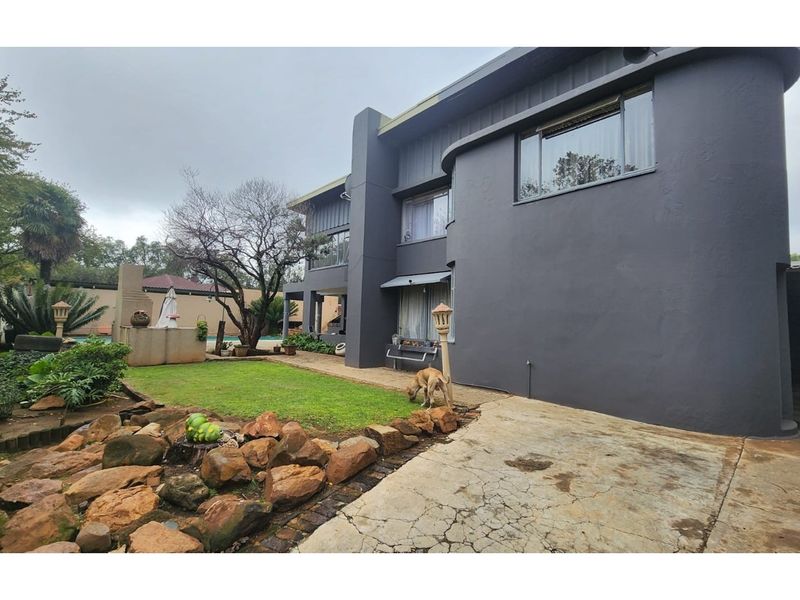 Rear exterior view of the property featuring a paved walkway, built-in braai area, and landscaped garden space.