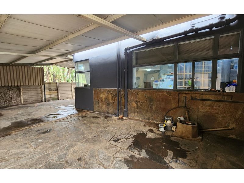 A covered outdoor patio area featuring stone-clad walls, paved flooring, and a metal roof structure, providing a functional space for outdoor utility or entertainment.