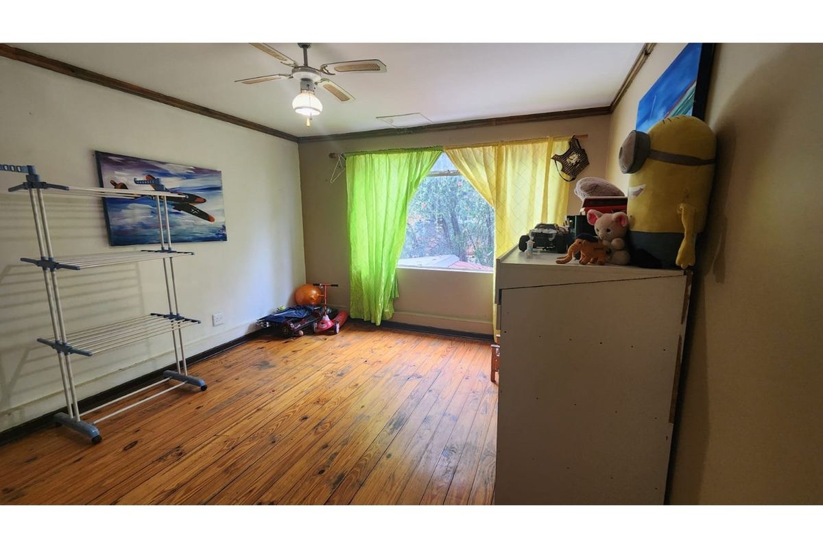 A bedroom featuring original timber flooring, a ceiling fan, and natural light from a window. The space requires cosmetic updates to improve its overall condition.