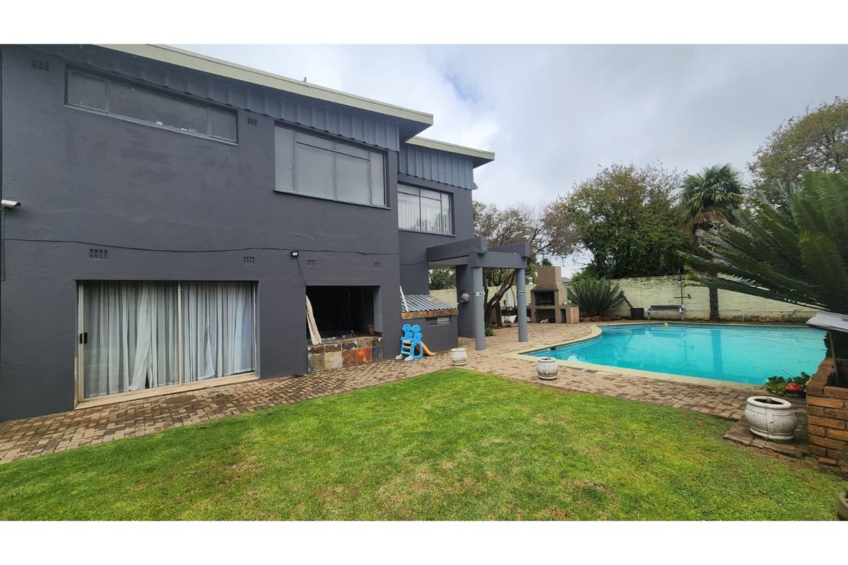 Rear exterior view featuring a swimming pool, paved patio area, and a built-in braai, set against a dark-painted double-story house facade.