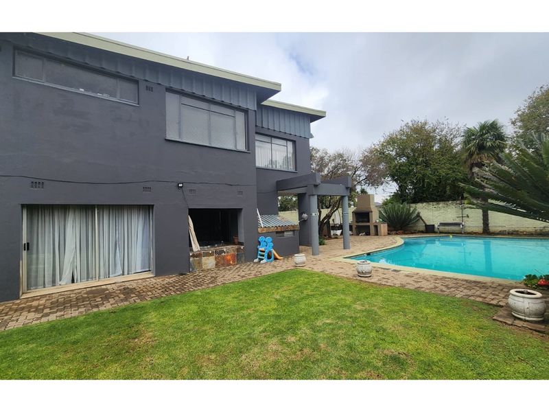 Rear exterior view featuring a swimming pool, paved patio area, and a built-in braai, set against a dark-painted double-story house facade.