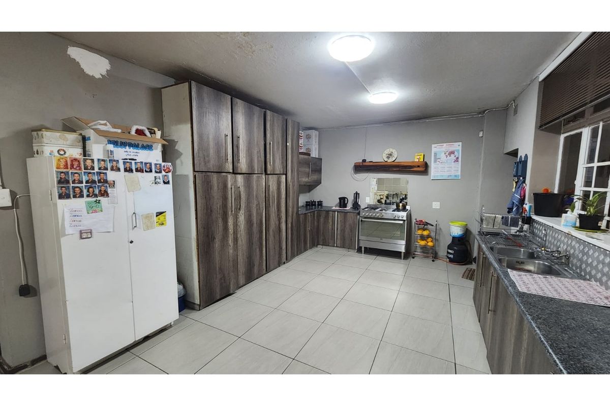 A functional kitchen featuring wood-look cabinetry, a gas stove, and double sink, with tiled flooring and potential for cosmetic updates.