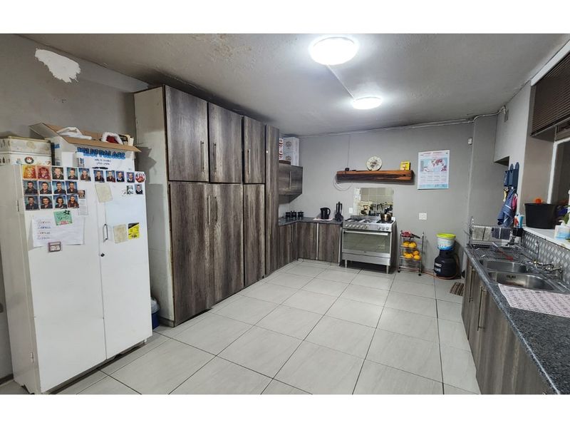 A functional kitchen featuring wood-look cabinetry, a gas stove, and double sink, with tiled flooring and potential for cosmetic updates.