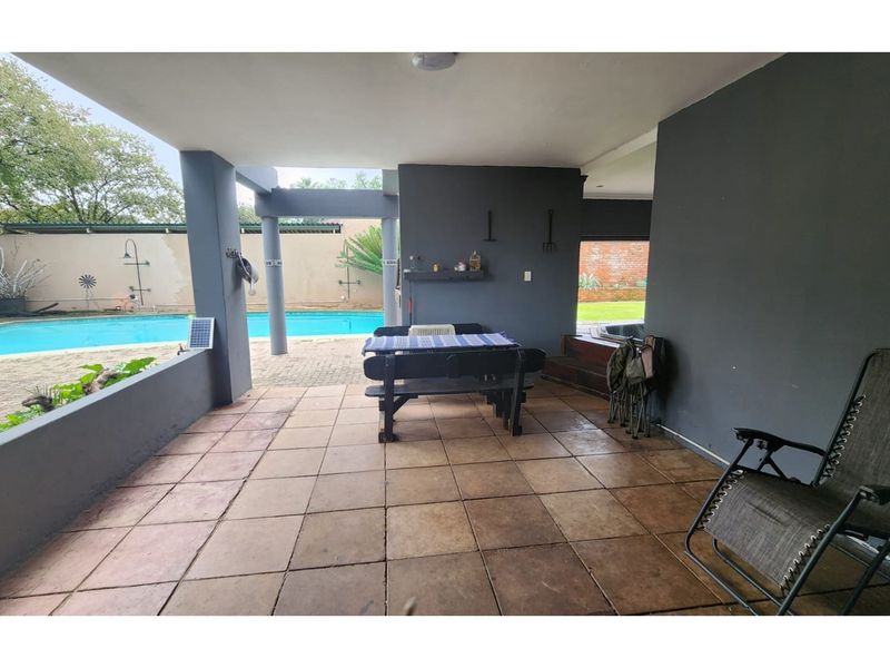 Covered outdoor patio area featuring tiled flooring and concrete pillars, overlooking a swimming pool and private garden space.