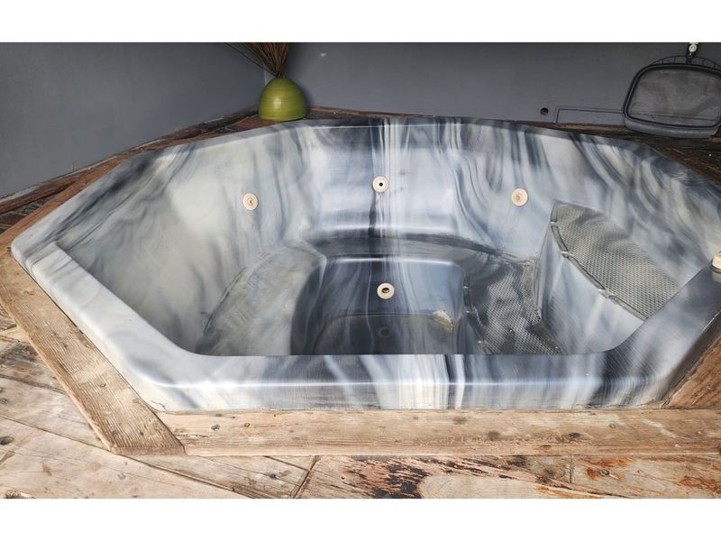 A built-in jacuzzi set within a wooden deck area, showing signs of wear and requiring maintenance.