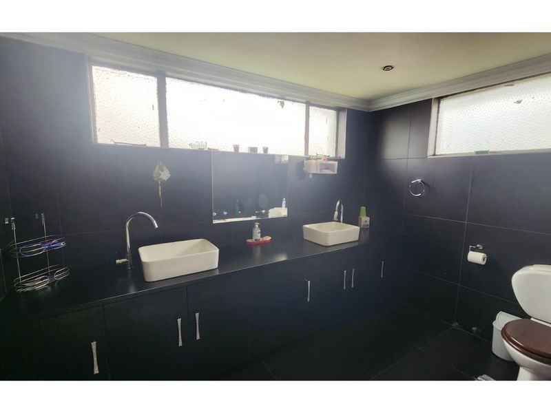 A modern bathroom featuring a double vanity with vessel sinks, dark tiled walls and flooring, and ample built-in storage cabinetry.