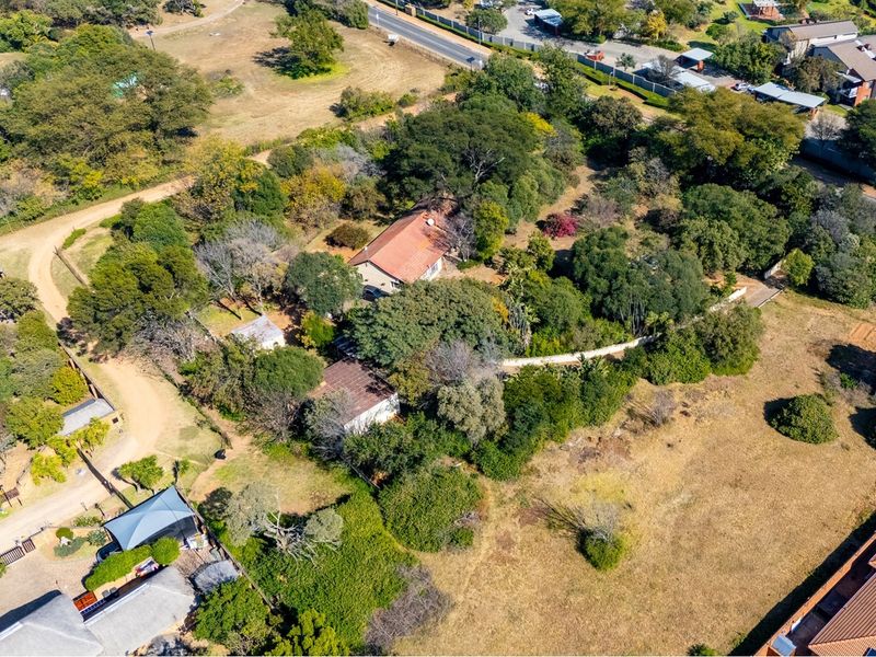 Aerial view of a residential property featuring established trees, a main dwelling with a tiled roof, and surrounding open land.