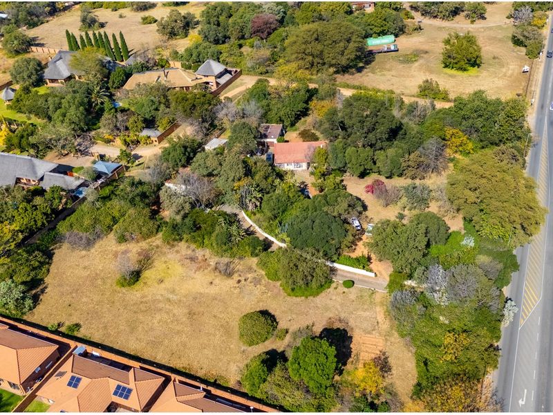 Aerial view of a large, tree-filled residential vacant land plot situated adjacent to a main road, featuring established vegetation and surrounding residential properties.