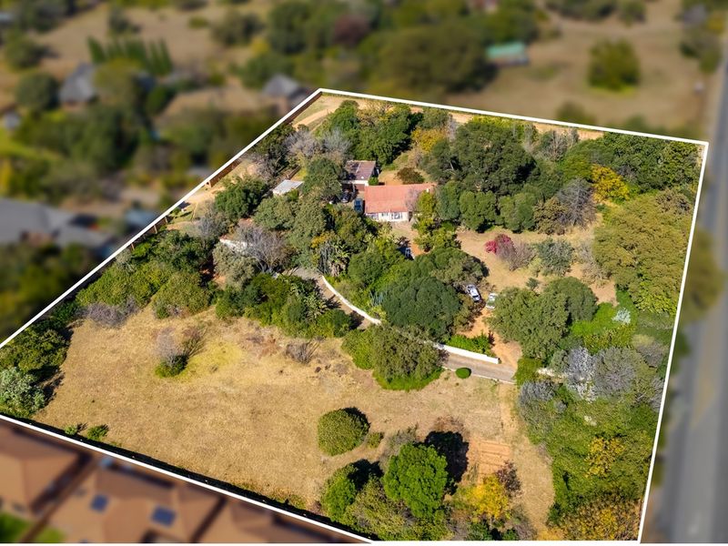 Aerial view of a large residential plot featuring established trees, a driveway, and existing structures set within a spacious, natural landscape.