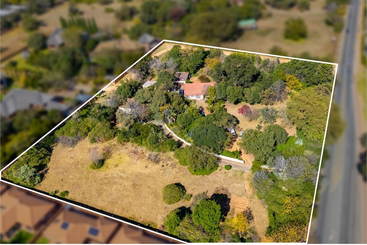 Aerial view of a large residential plot featuring established trees, a driveway, and existing structures set within a spacious, natural landscape.