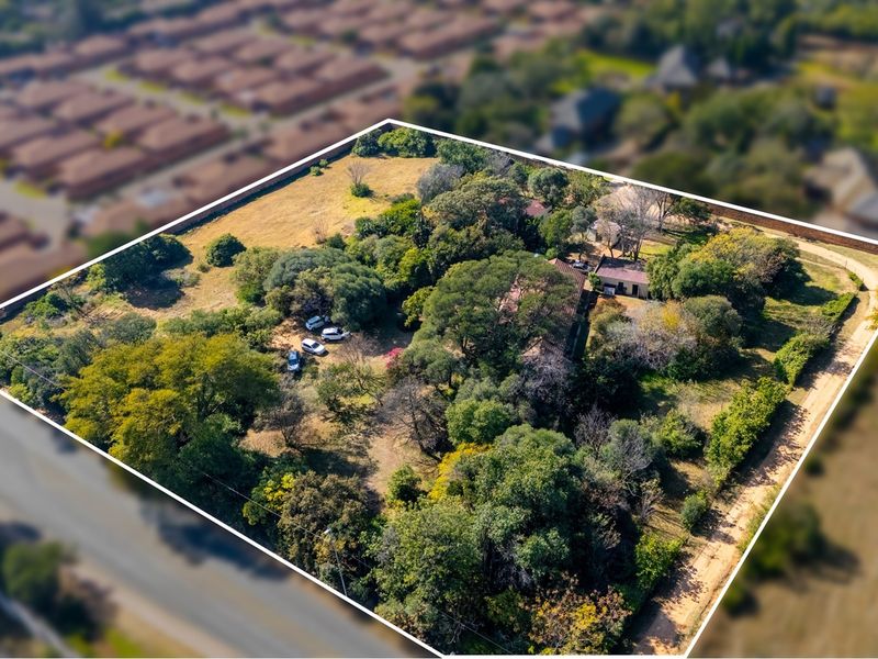 Aerial view of a large residential plot featuring mature trees, established vegetation, and existing structures within a suburban neighborhood setting.