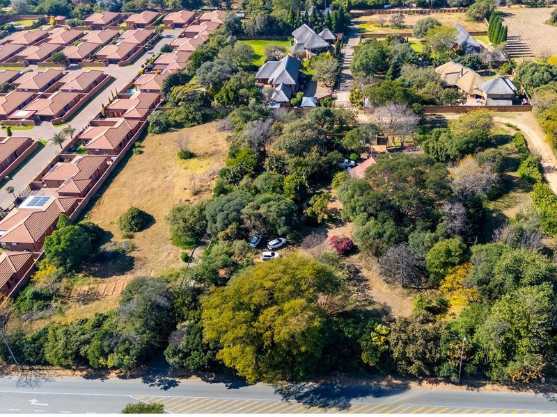 Aerial view of a large, undeveloped residential plot featuring mature trees and natural vegetation, situated adjacent to an established residential estate.