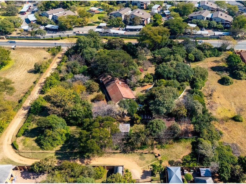 Aerial view of a residential property featuring a large, tree-filled plot with an existing dwelling and established garden surroundings.