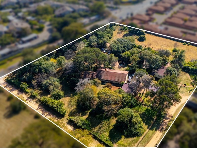 Aerial view of a large residential vacant land plot featuring mature trees, established vegetation, and existing structures on the property.
