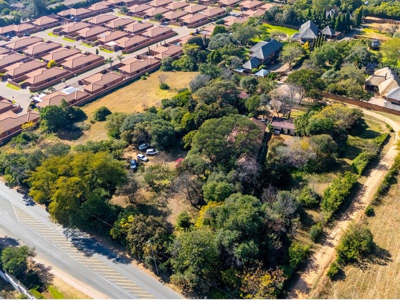 Aerial view of a large, tree-covered residential vacant land plot situated near a suburban housing development and main road access.