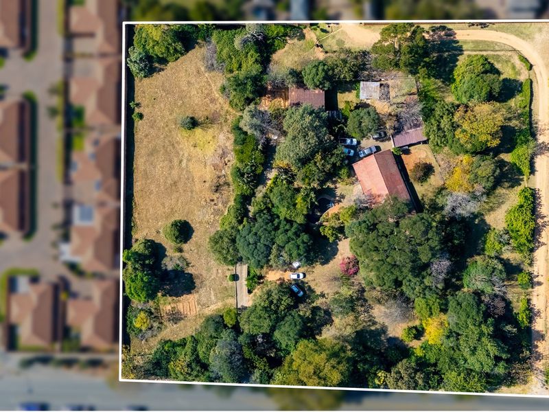 Aerial view of a residential vacant land plot featuring mature trees, established vegetation, and existing structures on the property.