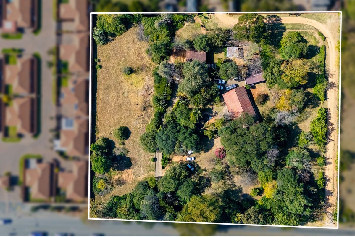 Aerial view of a residential vacant land plot featuring mature trees, established vegetation, and existing structures on the property.
