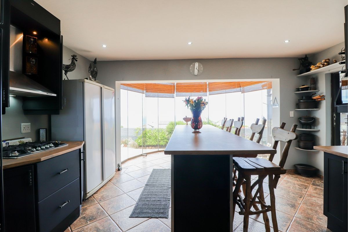 Modern kitchen featuring dark cabinetry, a built-in gas hob, extractor fan, and a central breakfast island, opening onto a glass-enclosed patio area.