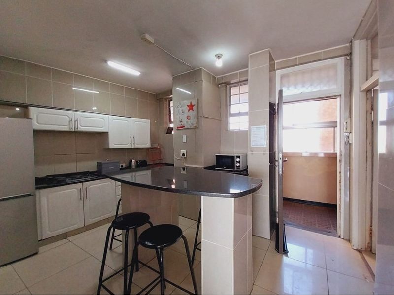 A functional kitchen featuring built-in cabinetry, a granite-topped breakfast bar, tiled flooring, and direct access to an adjacent balcony area.