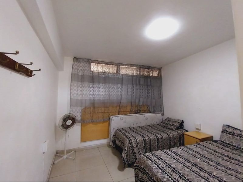 A functional bedroom featuring tiled flooring, a large window with fitted curtains, and wall-mounted coat hooks.