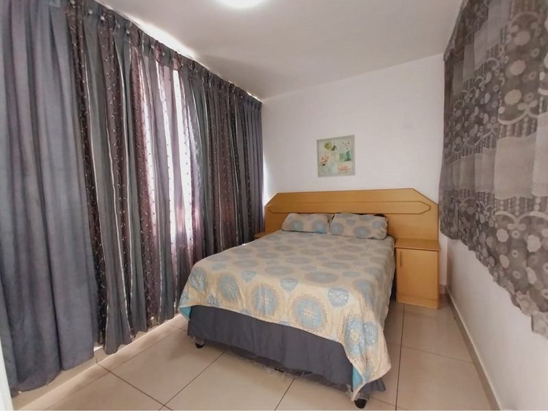 A bedroom featuring tiled flooring and a built-in wooden headboard with integrated bedside tables.