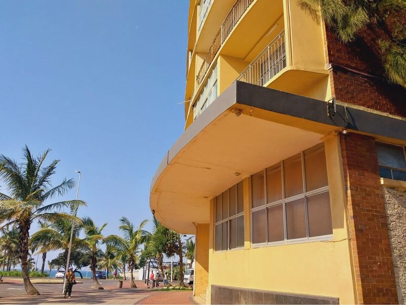 Exterior view of a multi-story apartment building featuring a prominent concrete overhang, brick masonry, and balcony access.
