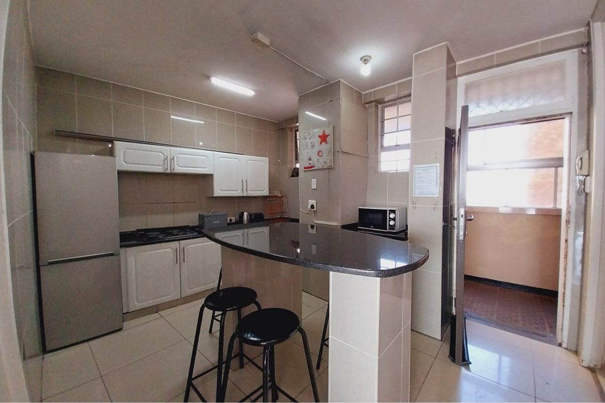 Functional kitchen featuring tiled walls and flooring, built-in cabinetry, a dark stone breakfast bar, and direct access to an outdoor balcony area.