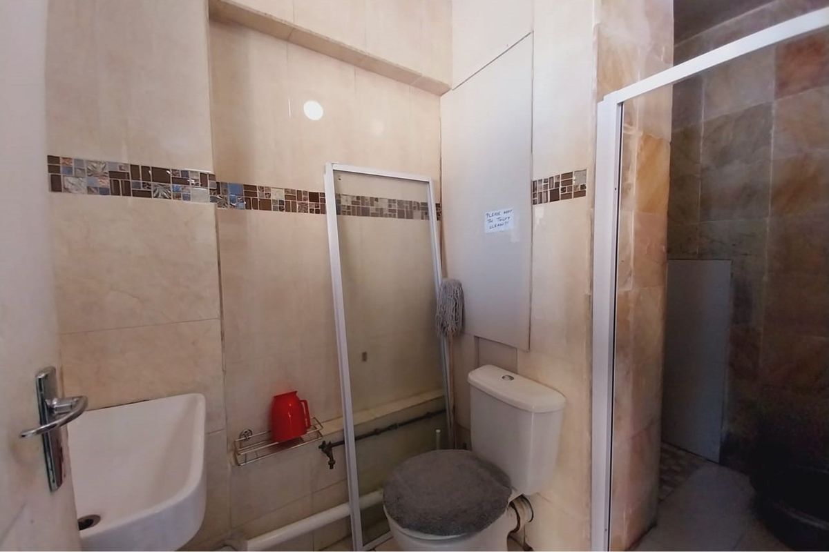 A compact bathroom featuring tiled walls with decorative mosaic accents, a standard toilet, and a wall-mounted basin with exposed plumbing.